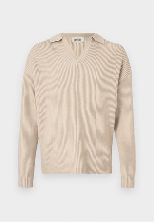 Beige ribba neulepusero, jossa on V-pääntie ja kaulus. Pitkät hihat ja rento istuvuus, valmistettu pehmeästä, rakenteellisesta kankaasta.