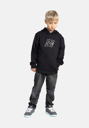 Zwarte hoodie met een groot wit logo, een kangoeroezak en een koord. Draagt bij donkere jeans en grijze sneakers met teal accenten.