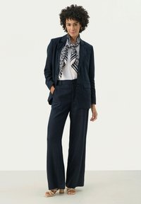 Navy linnen pak met een getailleerde blazer en wijde broekspijpen, gecombineerd met een witte top en een gebloemde sjaal in navy en wit.
