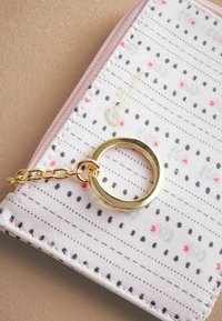 Portemonnee van een witte textuurstof met kleurrijke stippen, gouden hardware en een roze ritssluiter met een ketting en sleutelhanger bevestiging.