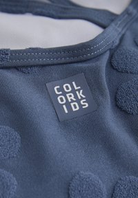 Marinblått tyg med mjuka, texturerade cirkulära applikationer och en rektangulär logotypetikett med texten "COLOR KIDS". Släta sömmar.