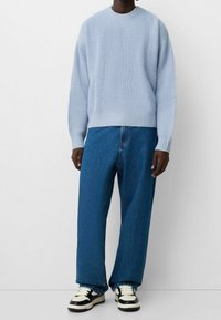 Pull tricoté bleu clair avec ourlet côtelé, associé à un jean bleu ample et des baskets noir et blanc. Une tenue décontractée et relax.