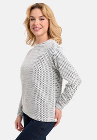 Helles graues Sweatshirt mit einem Rautenmuster, rundem Ausschnitt und langen Ärmeln, getragen über einer marineblauen Hose. Weicher Stoff und lässiges Design.