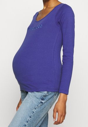 Paars geribd topje met lange mouwen en een ronde hals, met het woord "ASSISTED" in reflecterende letters op de borst.