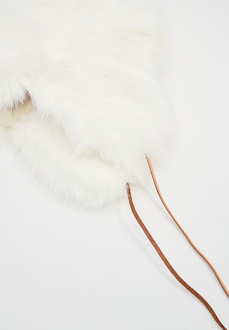 Weißes Kunstfell-Accessoire mit einer weichen Textur, versehen mit einem Lederband. Die Form ist rund und plüschig mit einer glatten Oberfläche.