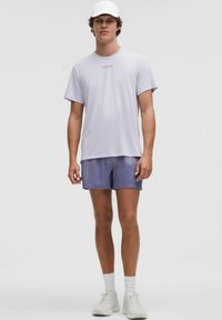 Ljuslila kortärmad t-shirt med en diskret logotyp, tillsammans med ljusblå shorts. Tillbehören inkluderar en vit keps och ljusa sneakers.