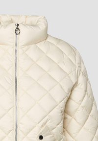 Jacket kremaste barve z rombasto šivanjem, srebrnim zadrgo, visokim ovratnikom in žepom na sprednji strani s pritisnim gumbom.