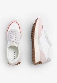 Bílé tenisky s růžovými semišovými detaily, šedými tkaničkami a červenými prvky. Pevná gumová podrážka s texturovaným vzorem pro lepší přilnavost. Logo na stélce.