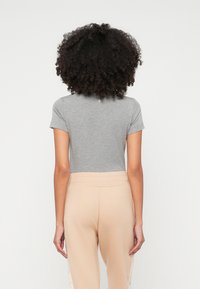 T-shirt grigio aderente con maniche corte, vista posteriore. Abbinato a pantaloni beige con dettagli testurizzati lungo i lati. Materiale in cotone liscio.