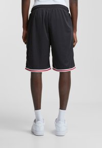 Pantalones cortos deportivos negros con ribetes a rayas rojas y blancas, cintura elástica y tela ligera, combinados con zapatillas y calcetines blancos.