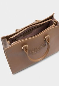 Braune synthetische Handtasche mit strukturiertem Finish, doppelten Griffen und geprägtem Logo. Der geöffnete Reißverschluss offenbart ein gemustertes Innenfutter.