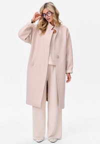 Lichtroze oversized jas van zacht materiaal, met een hoge kraag, enkele knoopsluiting en zijzakken. Gecombineerd met bijpassende wijde broek.