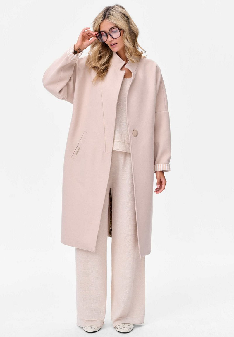 Lichtroze oversized jas van zacht materiaal, met een hoge kraag, enkele knoopsluiting en zijzakken. Gecombineerd met bijpassende wijde broek.