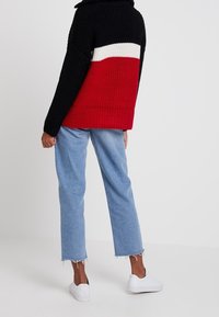 Tjock stickad tröja i svart, röd och vit, med hög krage. Kombinerad med ljusblå vida jeans och vita sneakers.