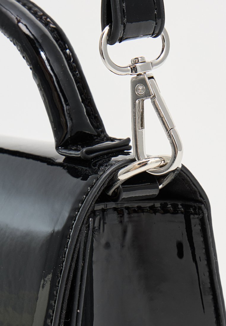 Sac à main en cuir verni noir avec une finition lisse et brillante, une poignée robuste, et un fermoir en métal argenté pour attacher la bandoulière.