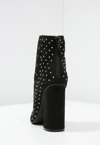 Schwarzer Wildleder-Stiefelette mit einem dicken Absatz, verziert mit silbernen Nieten und einem Reißverschluss an der Seite. Verfügt über eine glatte, strukturierte Oberfläche.