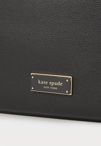 Black leather bag with a textured surface featuring a rectangular gold-tone hardware plaque that includes the brand name in white text.