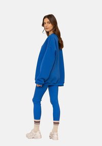 Przesadna niebieska bluza zestawiona z pasującymi niebieskimi legginsami. Miękka tkanina, luźny krój i okrągły dekolt. Srebrne sneakersy i paskowane skarpety.