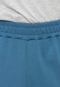 Κοντινό πλάνο ενός ανοιχτό γκρι πουκαμίσου που είναι βιδωμένο σε μπλε παντελόνια με ελαστική μέση, δείχνοντας την υφή του υφάσματος και τις λεπτομέρειες ραφής.