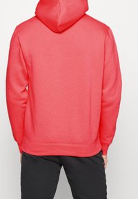 Sudadera de color coral con una capucha amplia, puños y cinturilla acanalados. Fabricada con una tela suave que presenta una textura lisa y un diseño sencillo.