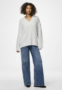 Šviesiai pilkas per didelis megztinis su V formos iškirpte, pagamintas iš minkštos medžiagos, derinamas su plačiomis mėlynomis džinsomis, turinčiomis nelygų kraštą ir laisvą siluetą.