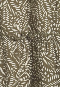 Tissu vert avec un motif de feuilles blanches, présentant une couture froncée et un bord festonné. Texture douce, apparence légère.