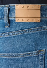 Plave traperice imaju kožni oznaku na struku s utisnutim riječima "TOMMY JEANS". Šivana obrada dodaje teksturu.