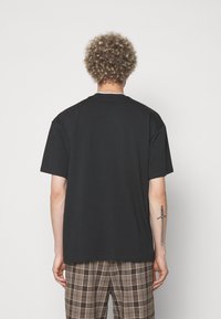 Svart bomullströja med avslappnad passform, rund halsringning och korta ärmar. Synliga sömmar och lätt textur, bärs med rutig byxor.