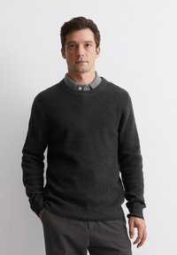 Dunkelgrauer gestrickter Pullover mit gerippten Bündchen und Saum, Rundhalsausschnitt, über einem grauen Hemd mit Kragen getragen, glatte Textur, taillierter Schnitt.