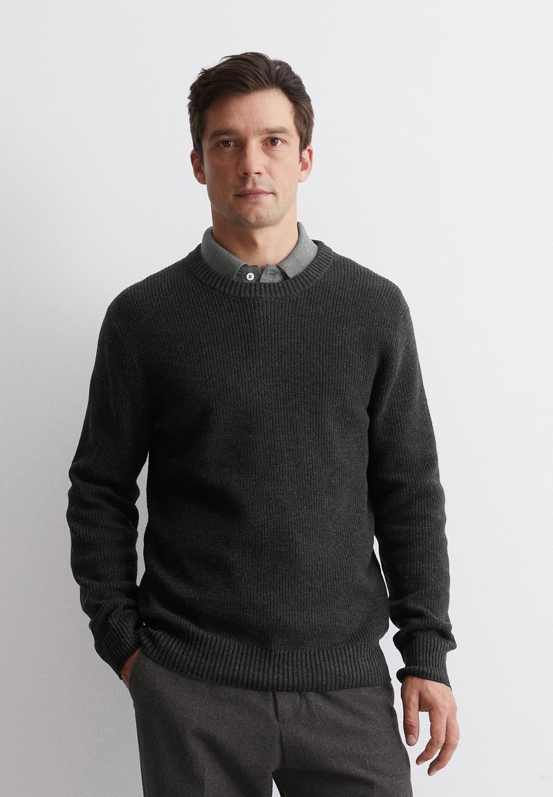 Dunkelgrauer gestrickter Pullover mit gerippten Bündchen und Saum, Rundhalsausschnitt, über einem grauen Hemd mit Kragen getragen, glatte Textur, taillierter Schnitt.