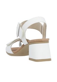 White heeled sandal featuring a strap with a buckle, soft interior lining, and a block heel. Smooth texture with a glossy finish.