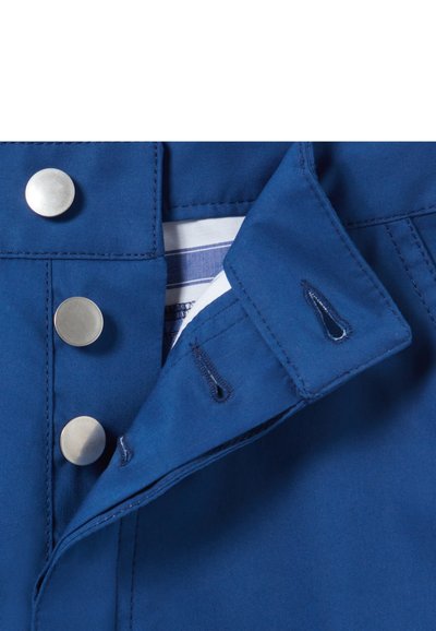 Tessuto blu con bottoni a pressione argento, caratterizzato da una pattina con colletto e dettagli ad occhiello. L'interno presenta una fodera a righe, offrendo un aspetto pulito e strutturato.