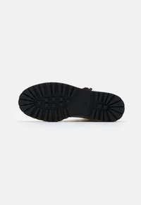 Semelle de chaussure en caoutchouc noir avec un motif de traction comprenant des croix et des lignes pour une meilleure adhérence. Bords lisses avec une texture structurée.