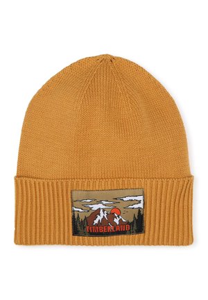 Bonnet tricoté jaune moutarde avec un poignet côtelé, présentant une écusson représentant des montagnes et un coucher de soleil, avec "TIMBERLAND" en lettres grasses.