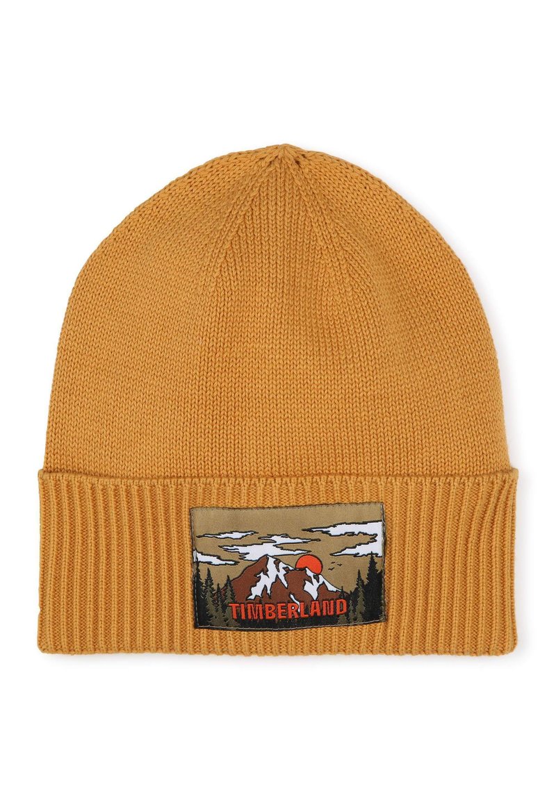 Bonnet tricoté jaune moutarde avec un poignet côtelé, présentant une écusson représentant des montagnes et un coucher de soleil, avec "TIMBERLAND" en lettres grasses.
