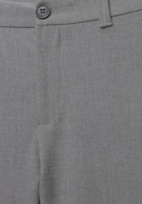 Gros plan d'un pantalon gris montrant la ceinture, la fermeture par bouton, les passants de ceinture et la texture du tissu.