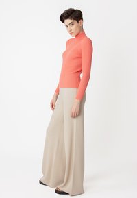 Korallenfarbener, gerippter Rollkragensweater kombiniert mit beige farbenen, weiten Hosen. Glatte Textur, eng anliegender Oberteil und lockere Silhouette im unteren Bereich.