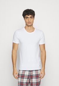 Weißes Baumwoll-T-Shirt mit rundem Halsausschnitt und kurzen Ärmeln, kombiniert mit karierten Schlafanzughosen in Rot, Blau und Weiß.