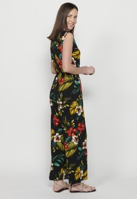 Tuta floreale con maniche corte, caratterizzata da uno sfondo nero e vivaci motivi botanici in rosso, giallo e verde; vita elastica.