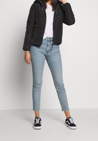 Doudoune noire à fermeture éclair et capuche, associée à un jean skinny bleu clair et des baskets noires avec des accents blancs.