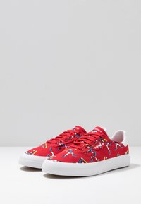Rote Leinensneaker mit mehrfarbigen Cartoon-Grafiken, weißer Gummisohle und Schnürsenkeln. Verfügt über ein flaches Profil und ein rundes Zehendesign.
