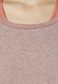 T-shirt à manches courtes et col rond en tissu marron clair chiné. Texture lisse avec un col intérieur en corail contrastant.