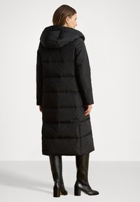 Garš melns pūkains mētelis ar kapuci, ar horizontālām kviltētām daļām, taisnu piegriezumu un sānu kabatām. Valkāts ar melnām augšstilbu garām zābakiem.