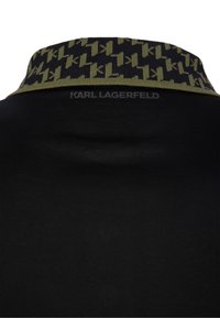 Černé polo tričko se vzorovaným zeleným límečkem. Na zadní straně je jemné černé logo. Hladká textura a přiléhavý střih.