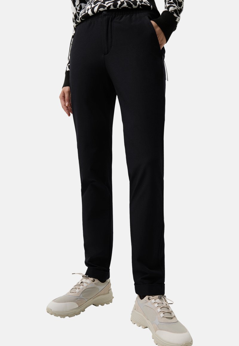 Schwarze Hose mit lockerem Sitz, ausgestattet mit einem elastischen Bund und Seitentaschen, kombiniert mit hellen Sportschuhen.