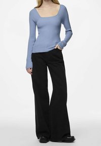 Haut bleu clair à manches longues côtelé avec un décolleté carré, associé à un pantalon noir à jambes larges et des chaussures noires.