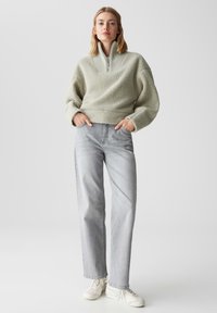Felpa in pile verde chiaro con colletto alto a costine, vestibilità comoda; abbinata a jeans dritti grigio chiaro e sneakers bianche.