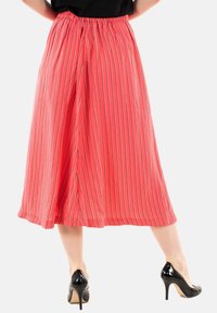 Falda midi coral con rayas verticales, cinturilla elástica y una silueta holgada, combinada con zapatos de tacón negros.