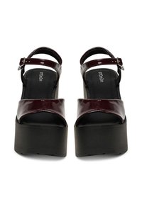 Bordové sandále na platforme z lakovanej kože s remienkom na členku, vybavené širokým predným pásom a hrubou čiernou podrážkou pre väčšiu výšku.