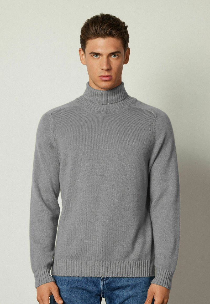 Grå stickad polotröja i mjukt material med ribbad krage och nederkant, med långa ärmar och en figurnära kropp.